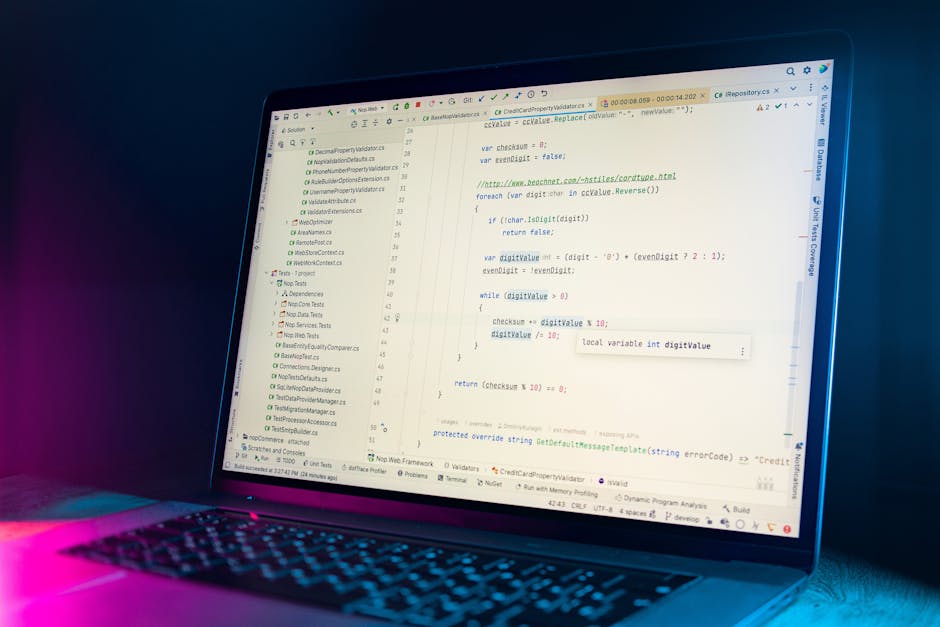 A close-up view of a laptop with a dark keyboard displaying a code editor on the screen, illuminated with blue and pink lighting against a dark background. The code appears to be written in a programm